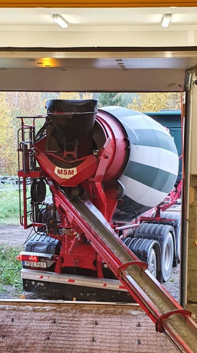 Betonblandare och utkörningsränna sett genom ett öppet garage vid gjutning av en betongplatta.