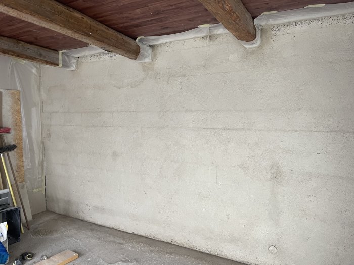 Nyputsad betongvägg i garage med träbjälkar och takisolering under arbete.