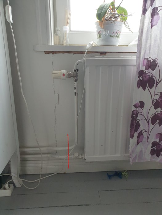 Vägg med spricka bredvid radiator under fönster med växt och gardin.