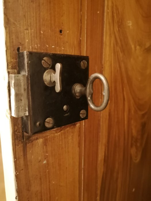 Gammal svart lås och nyckel på en brun träddörr, synliga slitage och patina.