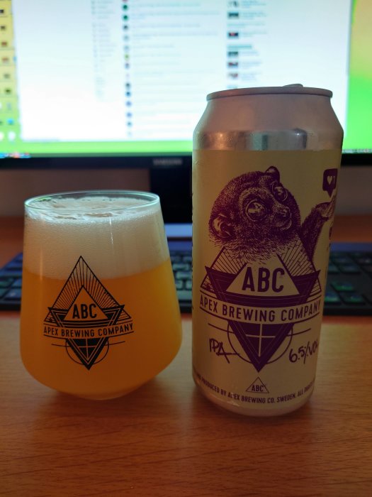 Ölglas med Apex Brewing Company-logotyp bredvid en ölburk med en apa och texten ABC.