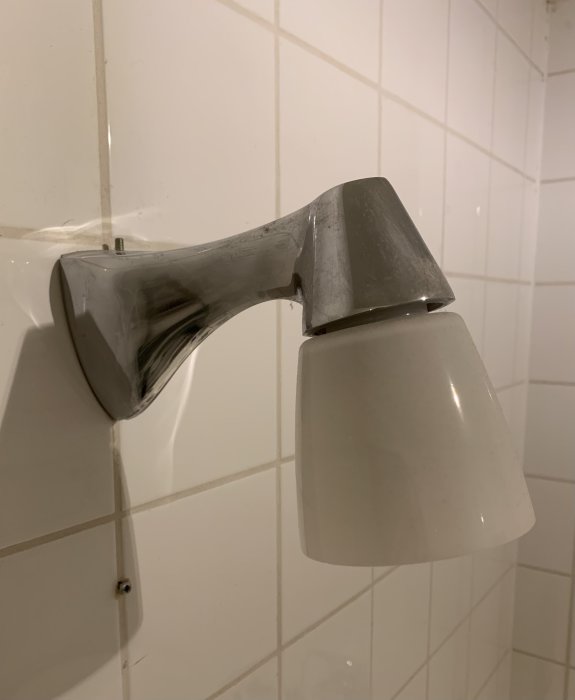 Närbild av en vit och kromad vägglampa på kakelvägg i ett badrum.