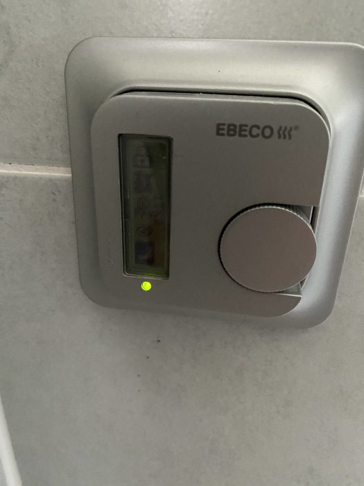 EBECO termostat på vägg med digital display och vridbart reglage, grönt funktionsljus tänt.