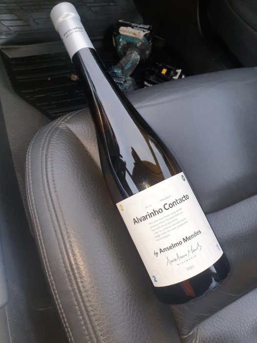 Flaska Alvarinho vin på bilens sittplats med öppen kartong och skräp i bakgrunden.