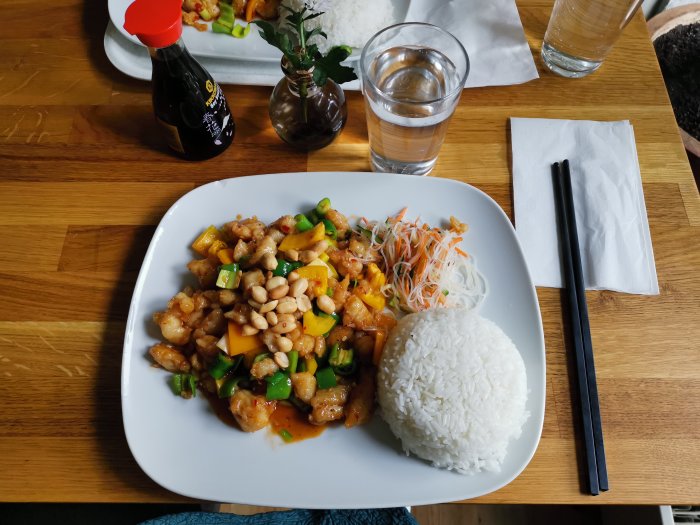 Tallrik med kinesisk Szechuan-rätt, en chili stark, serverad med ris och sallad på träbord.