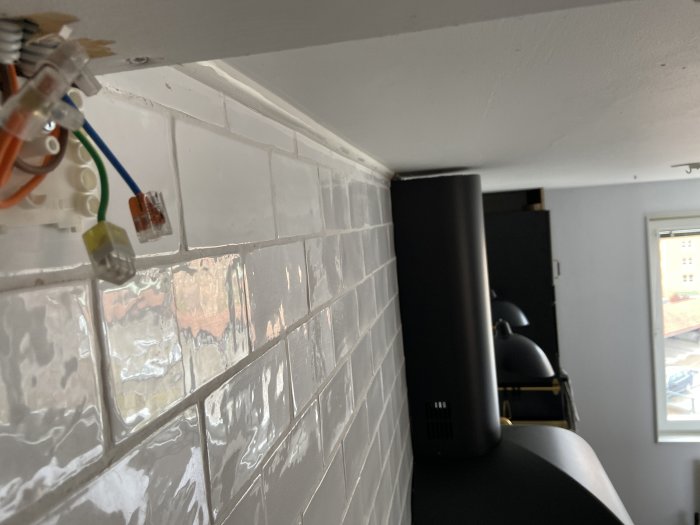 Elektriska ledningar med kopplingsdon vid ett hörn ovanför ett kaklat kök med synlig avluftningskåpa.