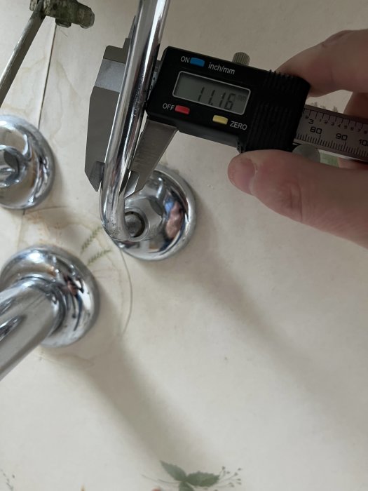Digital skjutmått visar 11.16 mm mätning på en kromad armatur.