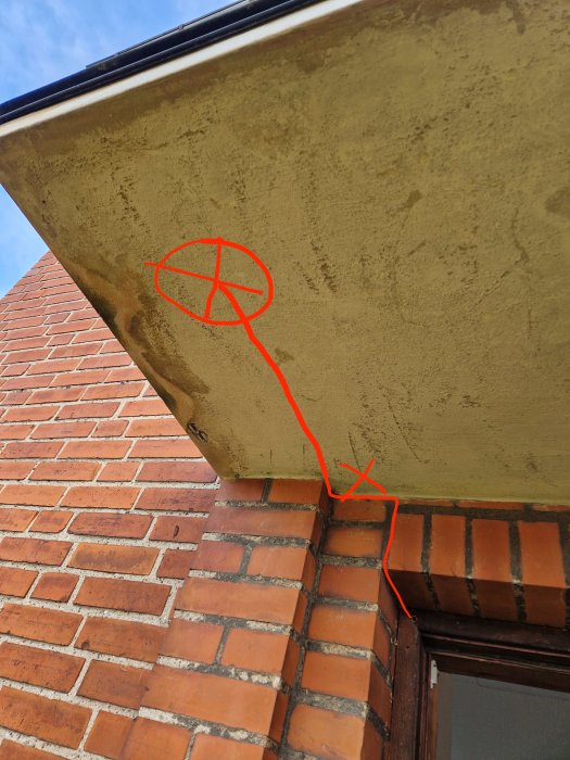 Problem med vattenavrinning markerat med röd pil på en huskant över ett tegelfönster.