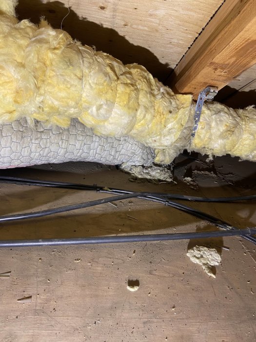 Isolerat grått rör som går genom vinden med synlig mineralullsisolering och elledningar.