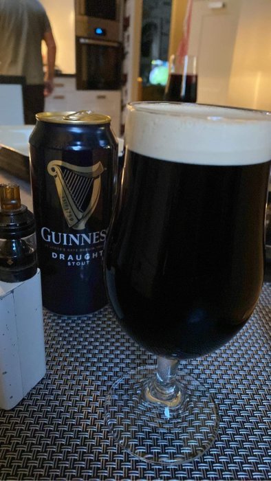 En burk Guinness och ett glas med mörk öl på ett bord, suddig bakgrund med någon som går.