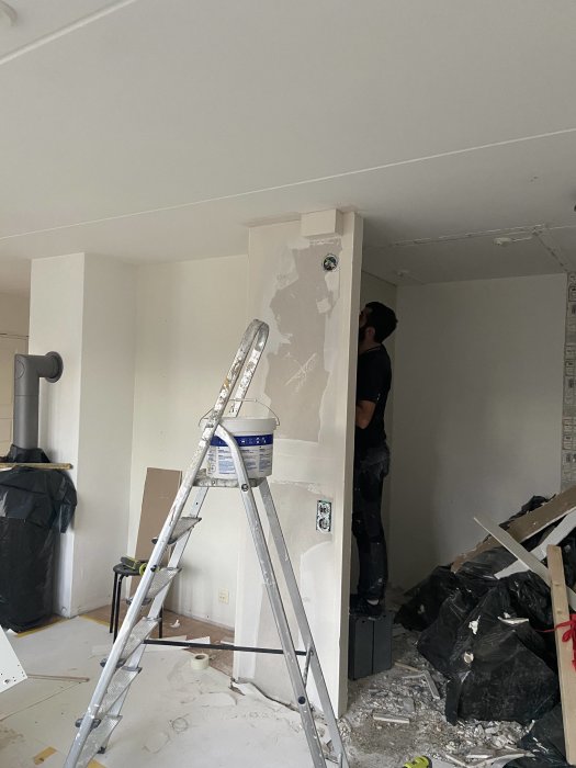 Renoveringsarbete med en person som målar väggen intill en spiskamin och en stege framför.