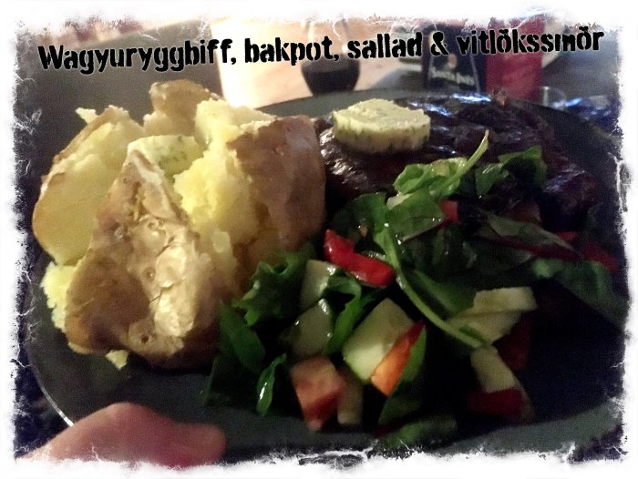 Wagyuryggbiff med kryddsmör, bakad potatis och en fräsch sallad på en mörk tallrik.