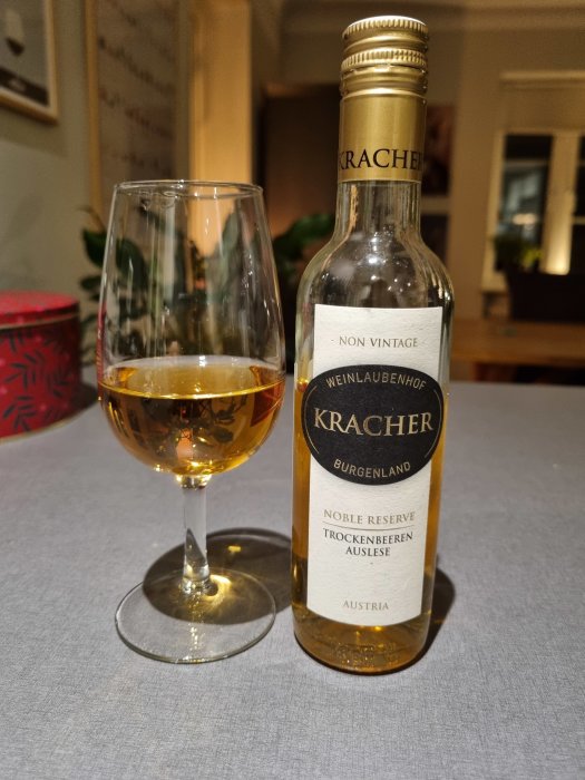 Flaska och glas med ädelrötad vin, Kracher Trockenbeerenauslese, på ett bord.