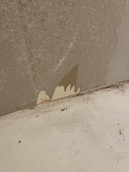 Skadad vägg med flagnande färg och puts, närbild vid golvkant.