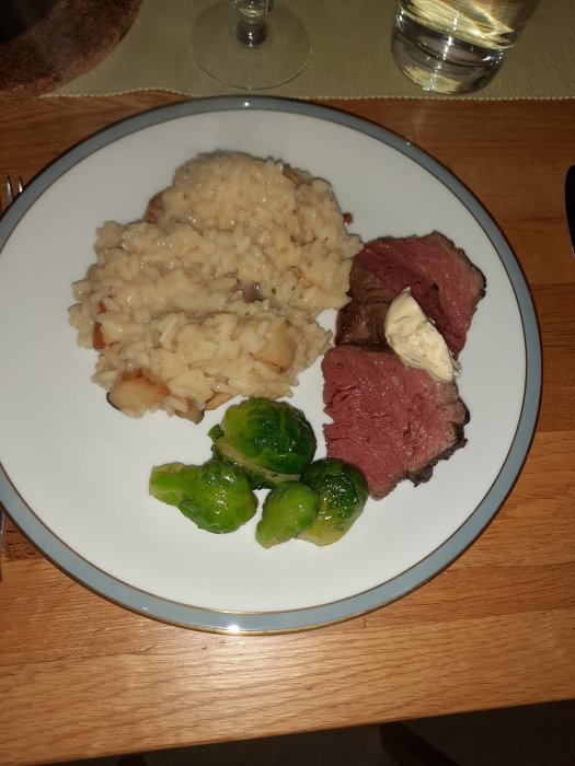 Risotto med Karl Johan svamp, lågtempererad rostbiff, brysselkål och klick chili smör på en vit tallrik.