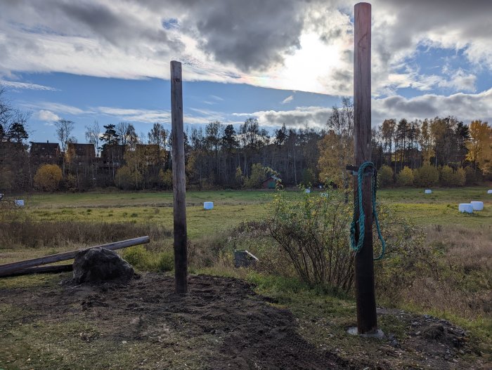 Två stolpar som står upp i en grävd och nyligen återfylld mark, förberedda för en gungställning.