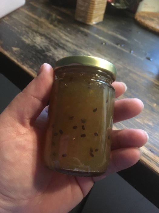 Hand håller en liten burk krusbärsmarmelad med chili, redo att avnjutas med ostkex.