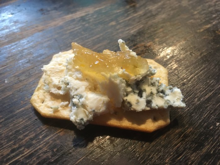 Ostkex med ädelost och krusbärsmarmelad på ett träbord.
