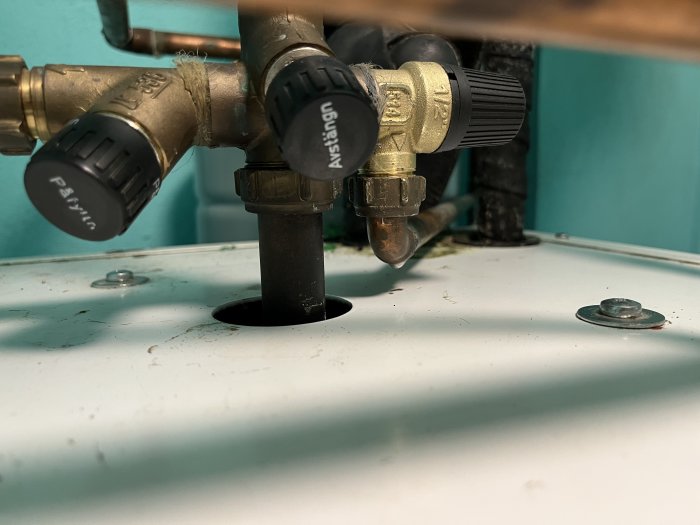 Vattenpump och säkerhetsventiler med lin och packningspasta applicerat, installerade över en vit yta.