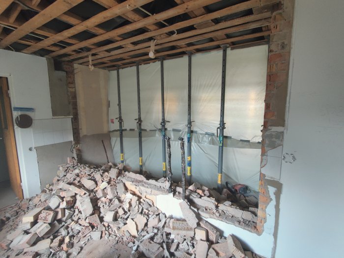 Renoveringsarbete med stödställningar och en hög av riven tegelsten i ett halvfärdigt rum.