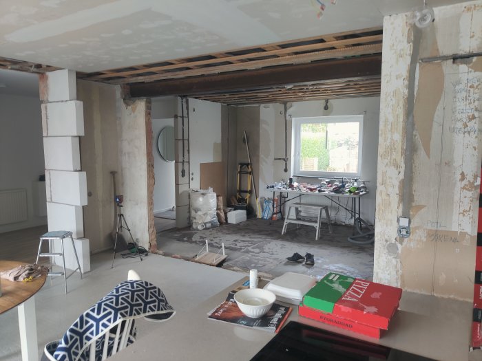 Ommöblerat rum under renovering med exponerade takbjälkar, byggmaterial och verktyg på golvet.