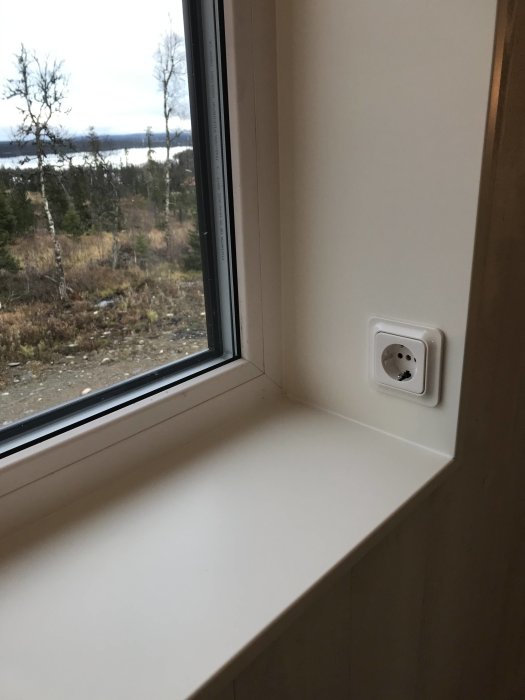 Färdigmålad MDF-fönsterbräda och väggsmyg installerade vid ett fönster med utsikt över landskap.