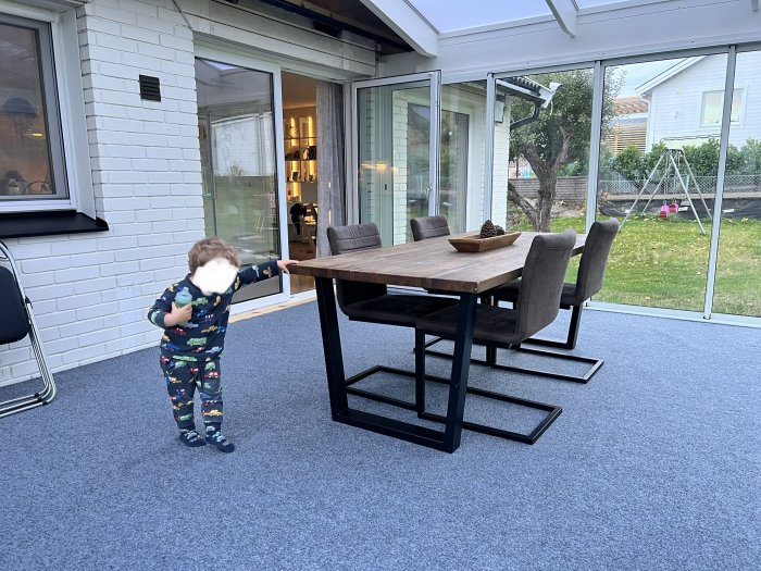 Inrett uterum med blå matta, matbord och stolar, samt ett barn som pekar mot eluttaget i hörnet.