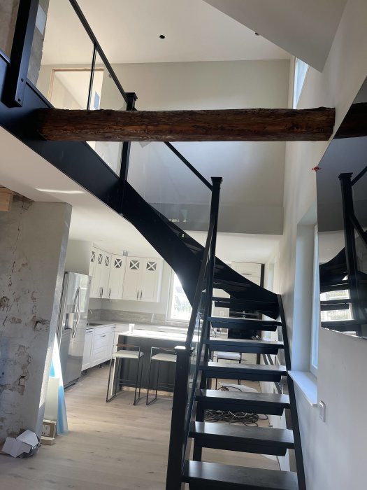 Svart trappa med glasräcken, tunna svarta rör och fyrkantiga stolpar i ett modernt kök.