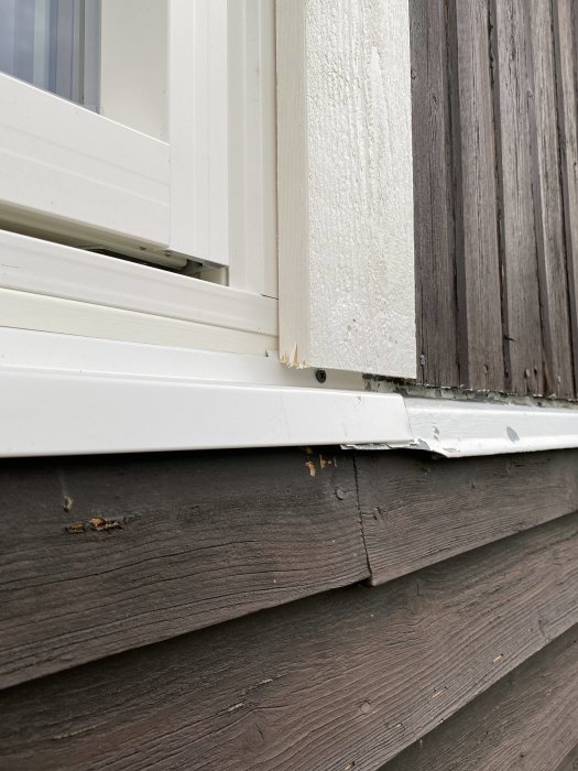 Detaljbild av fönster med plåtbleck nertill på en trävägg, där lister lagts ovanpå varandra.