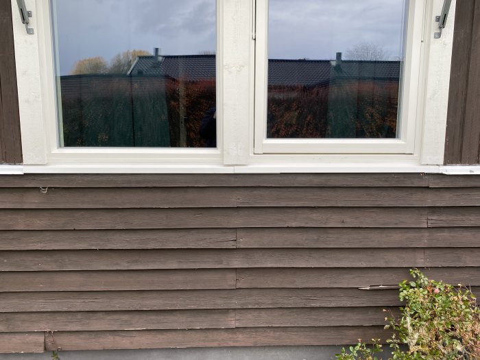 Fönster med vit karm och mörkbruna träpaneler med överlappande fönsterbleck nertill.