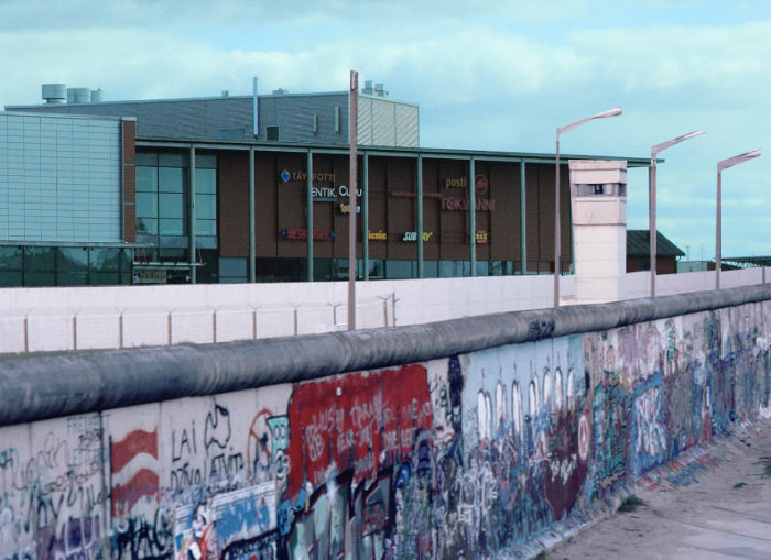 Bild av en mur med graffiti framför en byggnad, symboliserar restriktioner och gränser.