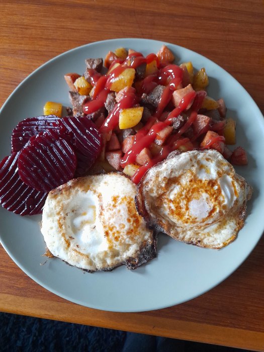 Tallrik med pyttipanna, stekt ägg och rödbetsskivor, toppat med ketchup.