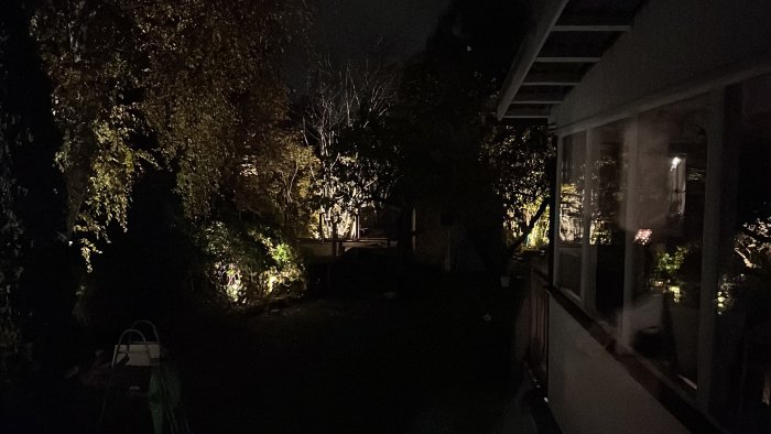 Upplyst trädgård på kvällen med installerad utebelysning i ett bostadshusområde.