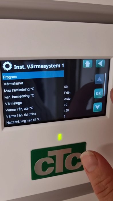 Digital display av en värmepump med inställningsmeny för värmesystem och en hand som pekar på skärmen.