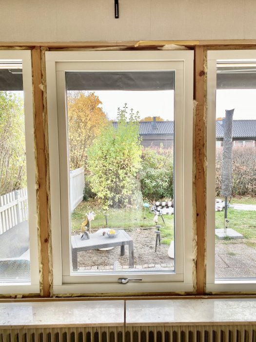 En överbelys bild av ett nyinstallerat fönster i ett vardagsrum med utsikt över en trädgård.