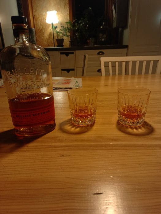 En flaska Bulleit Bourbon och två halvfulla whiskyglas på ett träbord som firande av Sveriges nya regering.