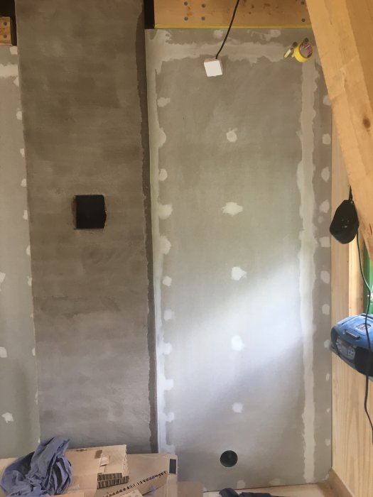 Vägg under renovering med spacklade och slipade ytor redo för målning, med byggmaterial synliga.