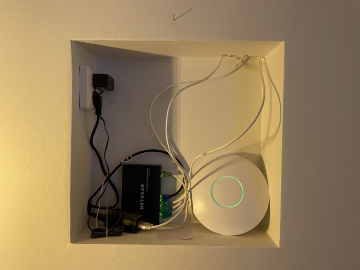 En nisch i en vägg med en router, olika kablar och en nätverksswitch placerade inuti.