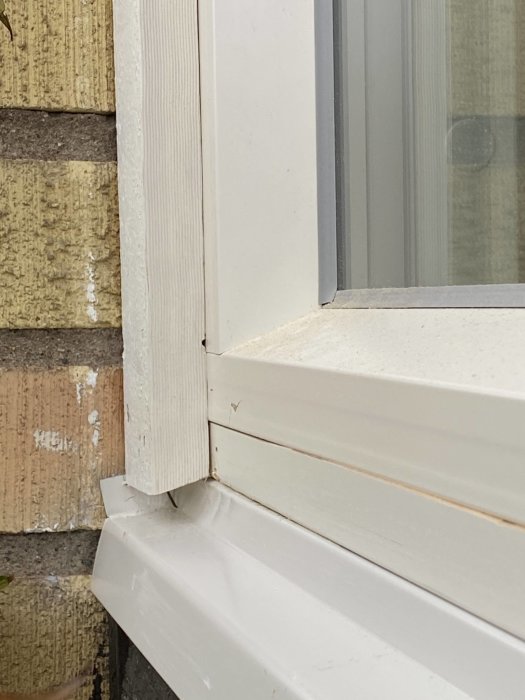 Närbild på fönsterhörn med lackat foder ovanför vit fönsterbleck vid tegelvägg, behov av högre montering av bläcket.
