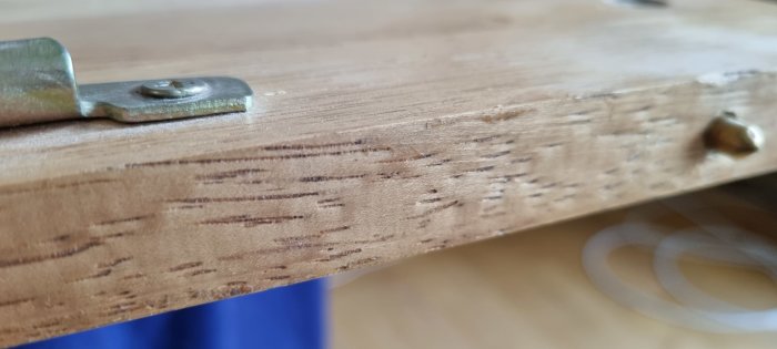 Närbild på en träyta med monterad metallbeslag och skruvar, tecken på användning syns.