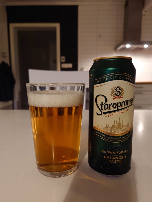 Ett glas öl bredvid en ölburk av märket Staropramen på ett vitt köksbord.