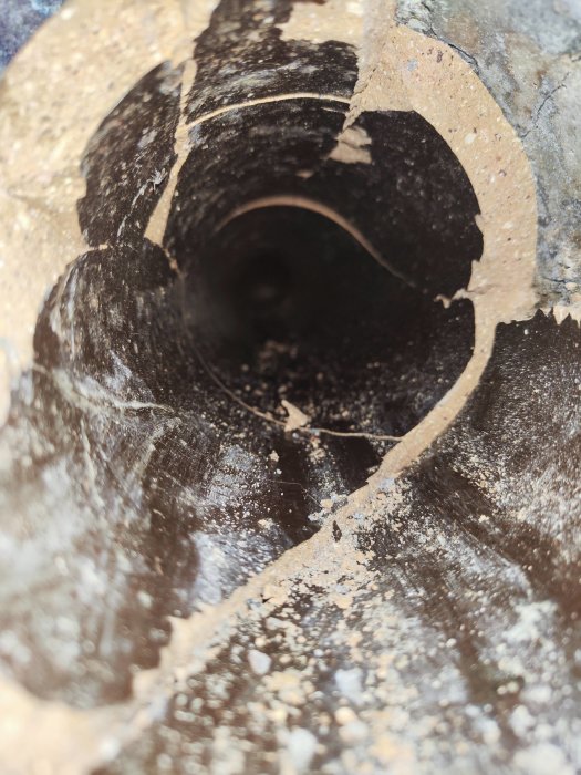 Närbild av ett borrat hål i betong med borrspån och damm runt öppningen.