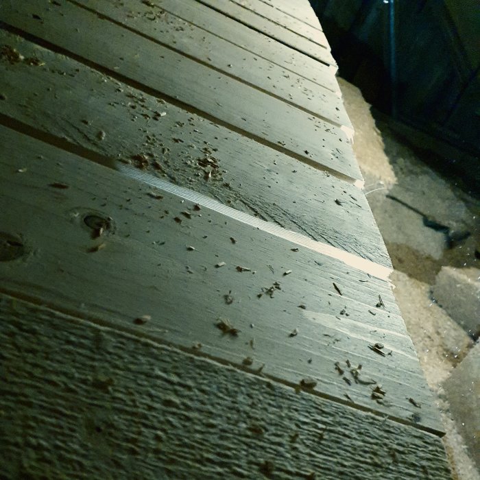 Träreglar lagda som golv på takstolar med synliga skruvar och lite spån.