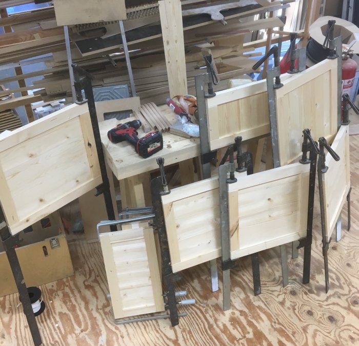 Träskåpsdelar i verkstad klämda i skruvtvingar, med verktyg och träspån omkring.