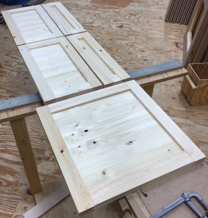 Trädelar för skåpstillverkning med frästa spår och limmade ramar på en arbetsbänk.