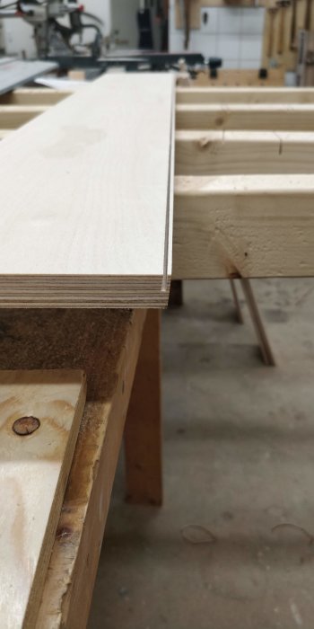 Närbild på träkonstruktion i en verkstad med träplattor och bottenplatta som har en snett sågad kan för att passa in i ett flyttbart skåp.