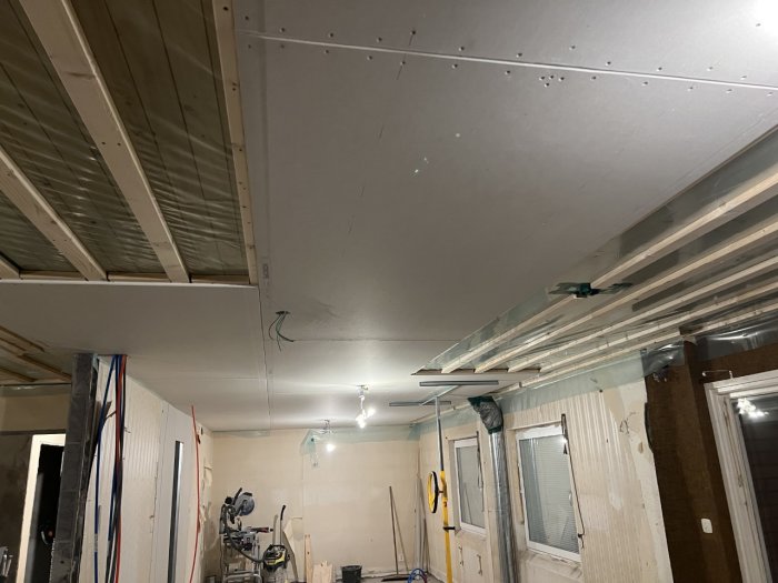 Gipstak under konstruktion i ett rum med installerade ventilationsrör och kanalfästen, samt exponerade träbjälkar.