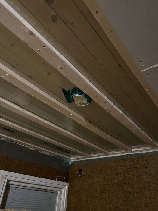 Ventilationsrör monterade i taket mellan träbjälkar med tejp och fästanordningar, i ett pågående byggprojekt.