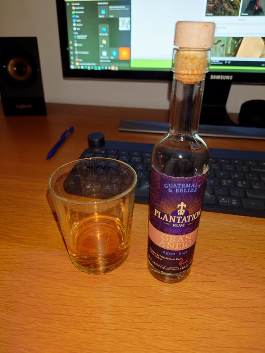 Flaska med Plantation Rum och ett glas med rom framför en datorskärm och tangentbord.