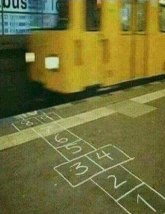 Gul spårvagn vid hållplats bakom ett hopp-spel ritat på trottoaren.